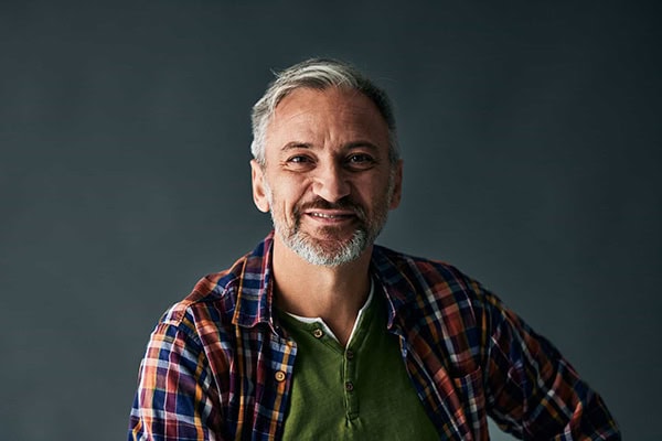 Grey-haired mature man, smiling for the camera, isolated on the grey background.